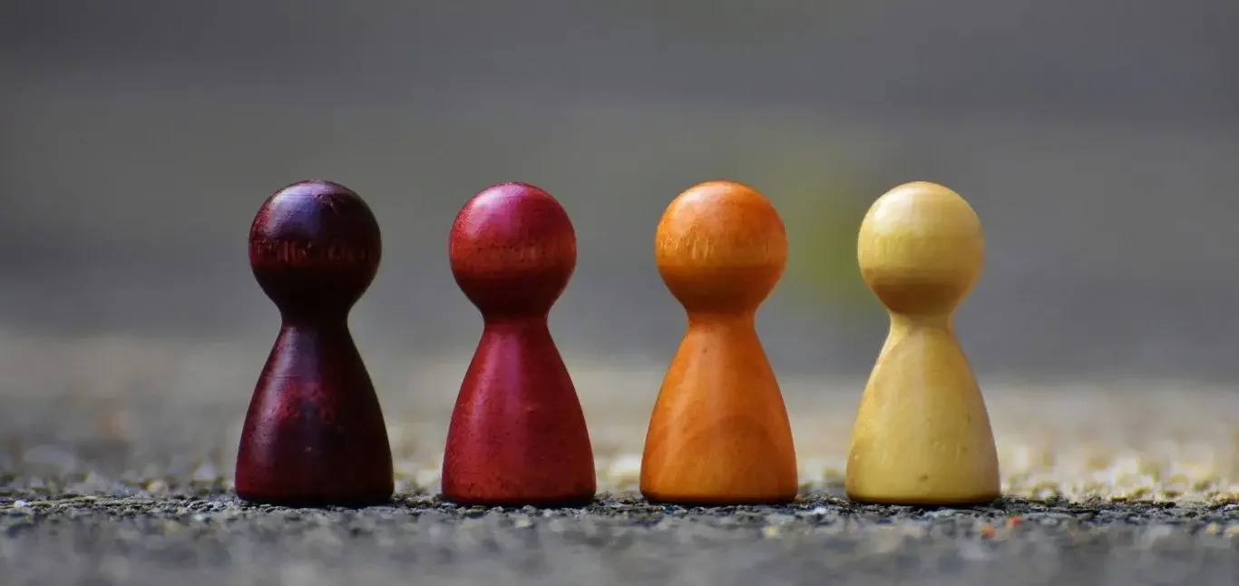 Four wooden game pieces in red, purple, orange, and yellow arranged in a row.